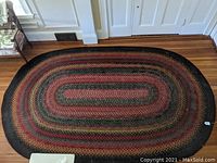 Full view of the large oval braided rug on a hardwood floor.
