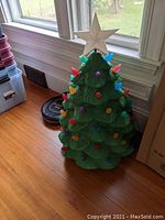 Full view of green plastic molded Christmas tree with colorful bulb lights and star top attached.