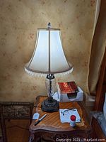 Pair of table lamps on wood side table, showing textured clear glass bodies, dark ornate metal bases, and beige fabric shades with crystal bead fringe trim.