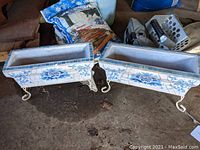 Pair of mosaic ceramic and cement planter boxes with blue floral design, white tile background, and metal curled legs.