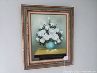 Full view of the framed oil painting showing white flowers in a blue vase on a yellow surface against a green background.