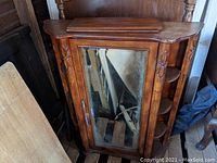 Front view of wooden medicine cabinet with mirrored door and carved side motifs