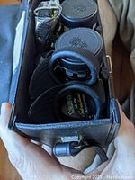Close-up image showing black Tasco Model 400 7x35 binoculars inside a carrying case, showing lens caps and branding.