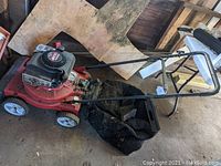 Full side view of the red Yard Machines lawn mower with attached black grass catcher bag and chipper attachment under handle.