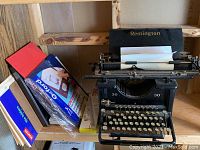 Remington typewriter on wooden shelf with various office supplies alongside including envelopes and writing pads.