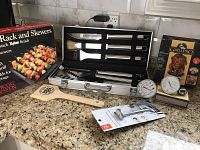 Photo showing boxed Royal Dining Rack and Skewers with non-stick nylon finish, GrillPro roasting accessory packaging, wooden spatula, and two dial thermometers placed on countertop.