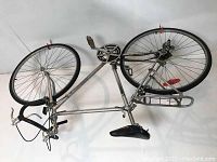 Silver frame road bicycle hanging on wall, showing full side view including wheels, pedals, and rear luggage rack.