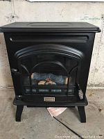 Front view of black electric stove heater with faux glass door and decorative logs inside.