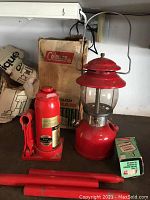 Photo showing red hydraulic bottle jack, Coleman camping lantern, and box of Coleman waterproof matches with packaging in background.