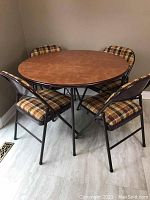 Set of round card table and four padded folding chairs shown together in room corner on a light tile floor.