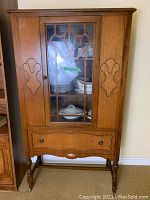 Front view of the antique china cabinet showing wood finish, glass door with muntins, and lower drawer.