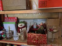 Photo of a shelf with plush snowman, glass candle holders, small glittery trees, and decorative box with floral picks and pinecones