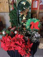 Full view of Christmas wreaths, swags, and floral picks displayed on a table and in a box, showing variety of colors and decorations