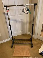 Full view of the clothing rack on casters with hangers and boot tray in front.