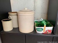 Three stoneware crocks of different sizes displayed side by side with a box of green glasses.