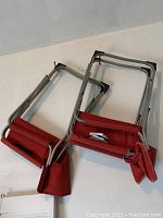 Two red folding lawn chairs lying flat folded on the floor, showing aluminum frames and packed red canvas seats.