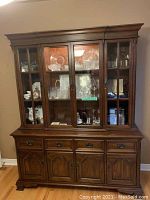 Front view of two-piece cherry wood hutch and buffet set with glass doors and storage compartments.