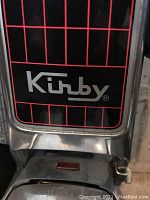 Close-up of Kirby branded front portion of vacuum cleaner showing metal construction and black/red grill design.