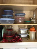 Top view of multiple plastic containers with blue lids and clear glass bowls with red lids, plus oil dispenser and shakers.