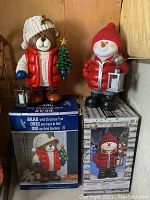 Photo showing both bear and snowman statues side by side with their respective boxes beneath them.