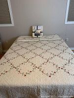 Quilt set spread on bed showing embroidered cream quilt with red flowers and green vines.