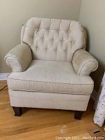 Front view of upholstered armchair showing neutral striped upholstery, button tufted backrest, and dark wood legs.