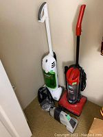 Photo showing three vacuum cleaners side by side; white Eureka Superlite with green container, red and black upright vacuum, and small handheld vacuum on the floor