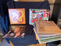 Photo showing collection of vinyl albums including 'Dimensions', 'Minipops', Elvis Presley album, and several others stacked.