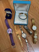 All eight pieces arranged together on wood floor: six watches, Birks bracelet and carved ring