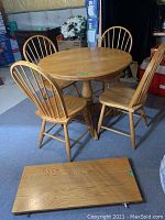 Overall view of solid oak round pedestal dining table with four matching chairs around it and one removable leaf piece placed in front.
