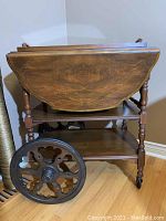 Side view of wood tea wagon showing larger front rubber wheels with decorative spokes and smaller rear wheels, drop-leaf top folded down.