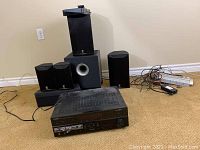 Yamaha AV receiver and 6 speakers including subwoofer on carpeted floor, power strip and cables in background.