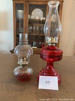 Two antique glass oil lamps on table, one red with octagonal base, one clear with round hobnail base.