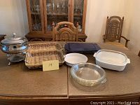 Overview of all baking dishes and chafing dish displayed on wooden table with dining chairs in background