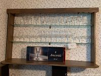 Two glass shelves with assorted clear bar glasses plus a boxed set of 6 Ancenis glasses (26 cl) displayed on a wooden frame against floral wallpaper.