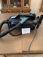 Black and blue handheld car vacuum with a blue handle and coiled power cord visible, placed on a wooden table.