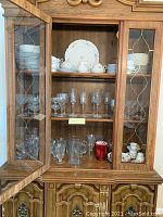 Wood china cabinet containing china and glassware, showing multiple shelves with dishes and glasses