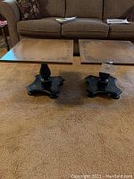 Two small square coffee tables side by side on a carpet, showing their light wood stenciled tops and black pedestal legs with curved bases.