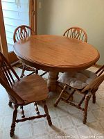 Oval wooden dinette table with four matching chairs arranged around it, showing wood grain and finish.