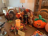 Resin turkey figurine, wooden turkey, fabric pumpkins, fall flower arrangements, and flameless candle on table