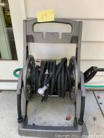 Black garden hose neatly wound on a grey plastic hose rack with handle and crank.