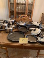 Overview of assortment of pots, pans including griddle on wooden table showing variety of sizes and materials.
