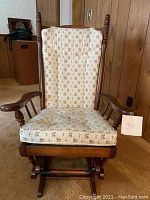 Front view of padded floral-patterned rocker/glider chair showing cushion and wooden armrests.