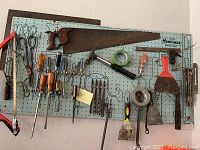 Photo of a pegboard with various hand tools including a crosscut saw, scissors, screwdrivers, chisels, paint scraper, and putty knife.