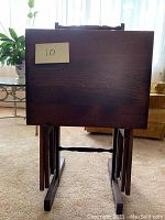 Front view of folded single TV tray on wooden stand with a label '10' attached.