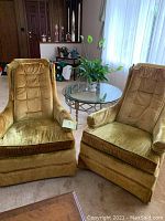 Pair of gold velvet upholstered armchairs with tufted backs and skirted bases shown together in living room.