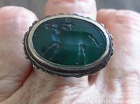 Top view showing green oval intaglio stone with animal carving on ring worn on a finger.