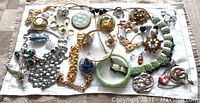 Photo showing a laid out assortment of various costume jewelry items including earrings, bracelets, brooches, rings, and pendants.