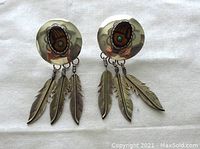 Front view of the pair of large sterling silver earrings showing the detailed engraved feathers, central turquoise bead, and enamel bear paw design on the domed stud base