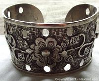 Front view of the wide floral embossed sterling silver bangle bracelet showing stippled background and circular cutout pattern.